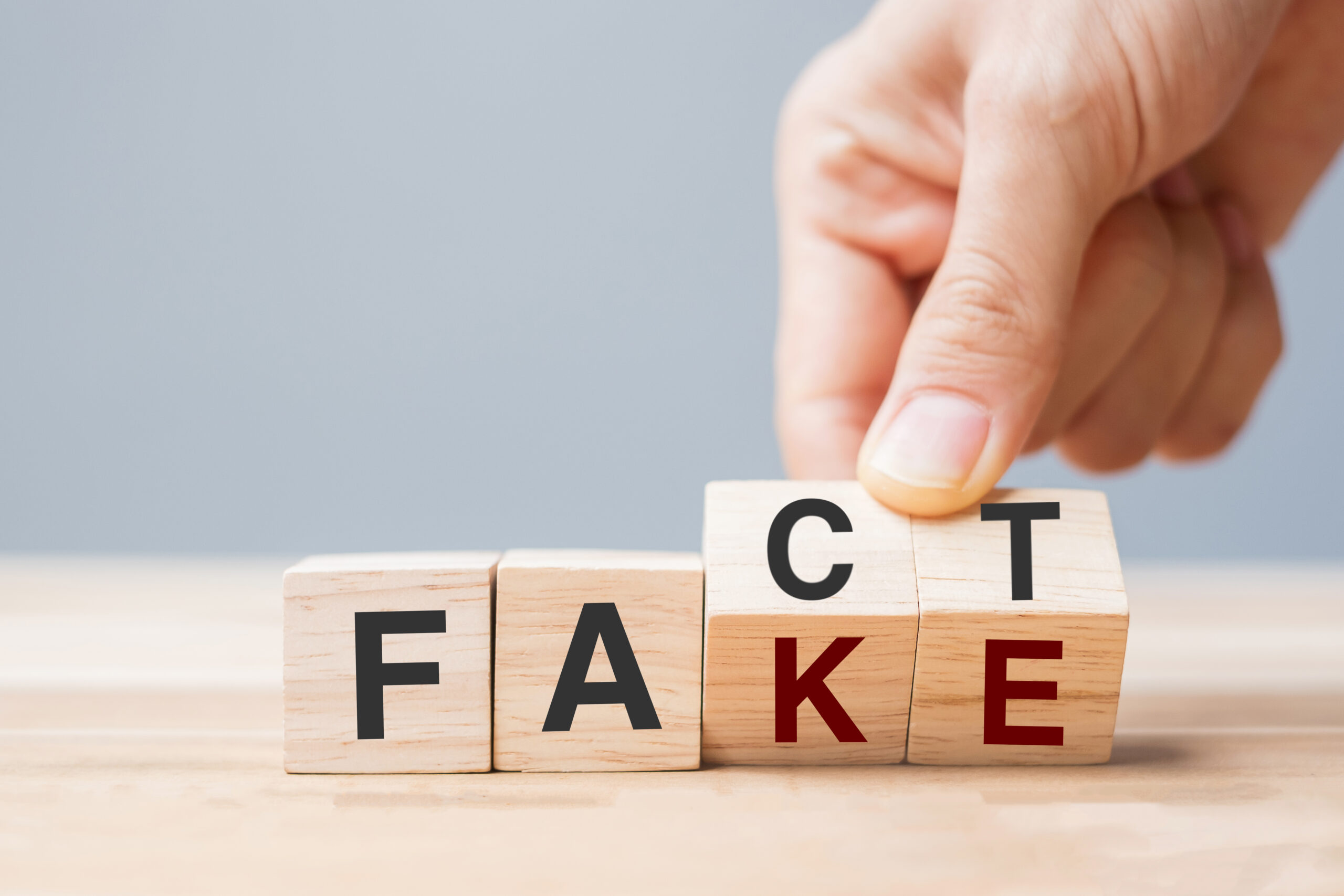 Wooden letter blocks spell out the word “FACT,” but the tilted C and T partially flip, making the word appear as “FAKE.